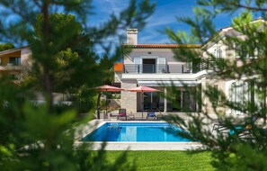 Una casa de dos pisos con piscina, mobiliario de exterior y jardín.