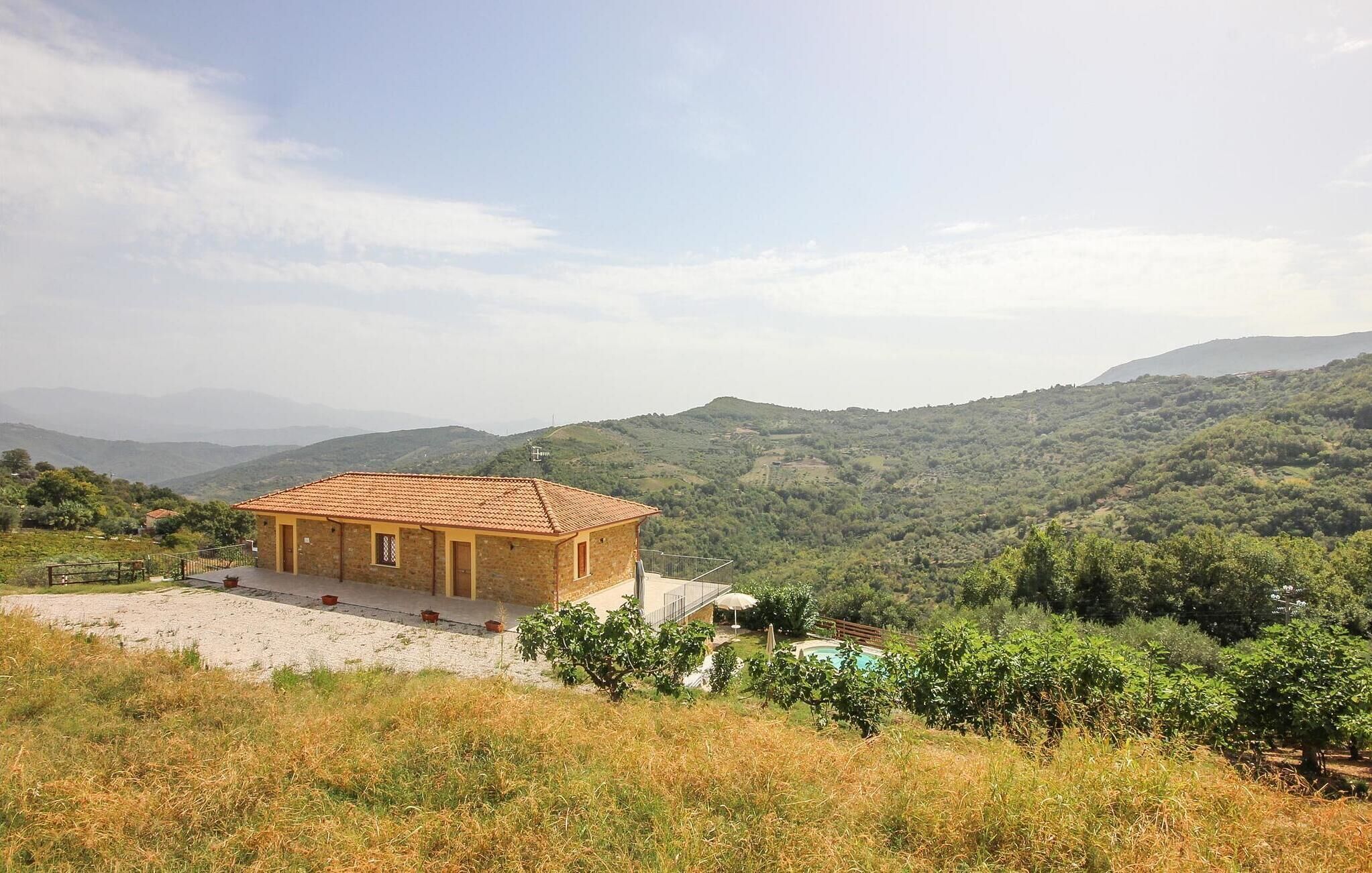 A small building with a tiled roof, surrounded by a gravel path and a pool, set against a backdrop of rolling hills and a clear sky.