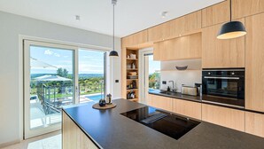 Una cocina moderna con una isla grande, electrodomésticos integrados y vistas a una piscina y al paisaje.