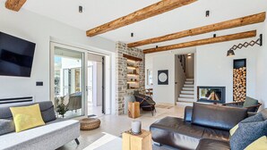 Una sala de estar moderna con una pared de piedra, vigas de madera, chimenea y una escalera.