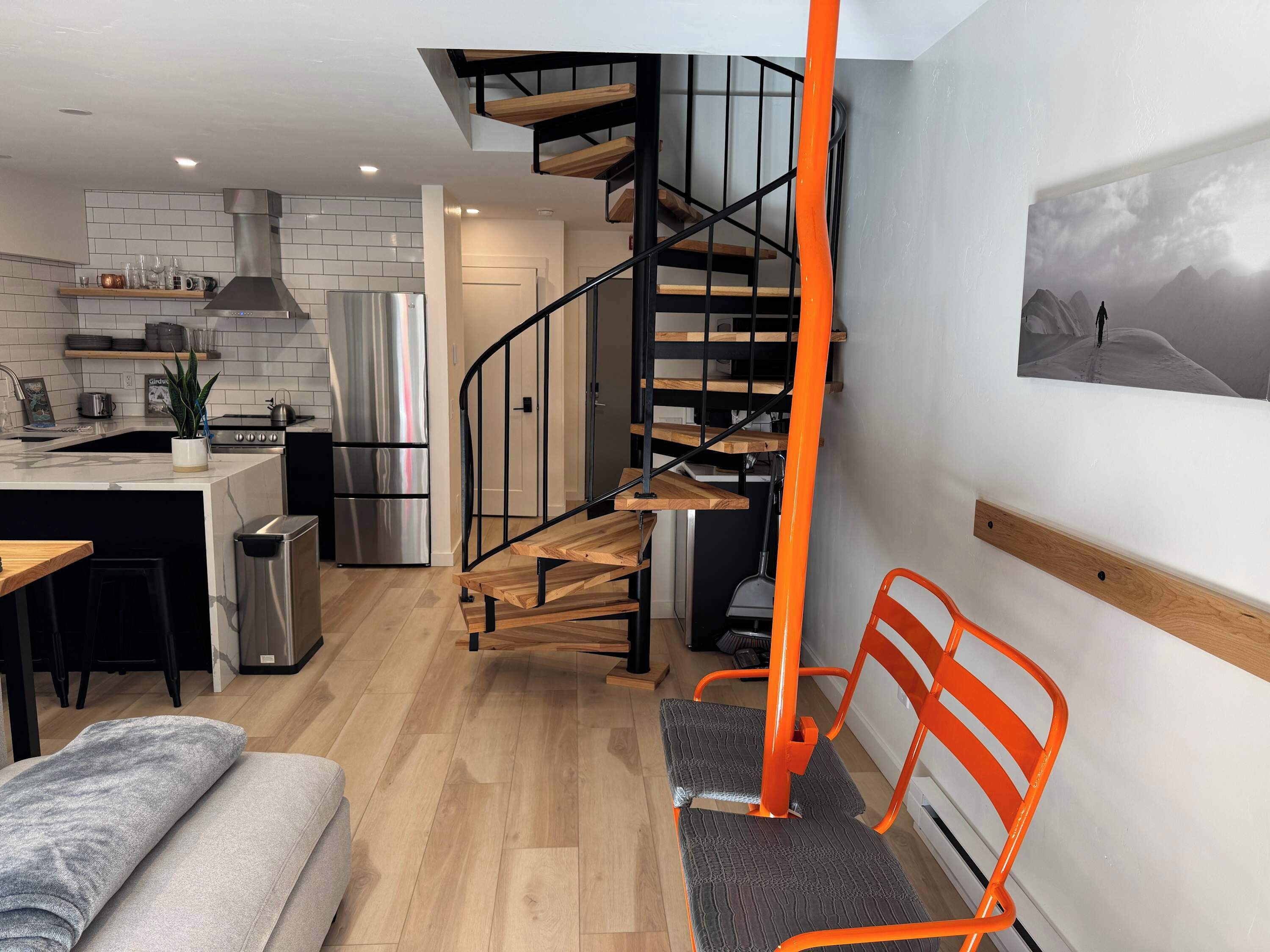 Een moderne keuken met een centraal eiland, een roestvrijstalen koelkast en een houten trap naar een hoger gelegen verdieping.