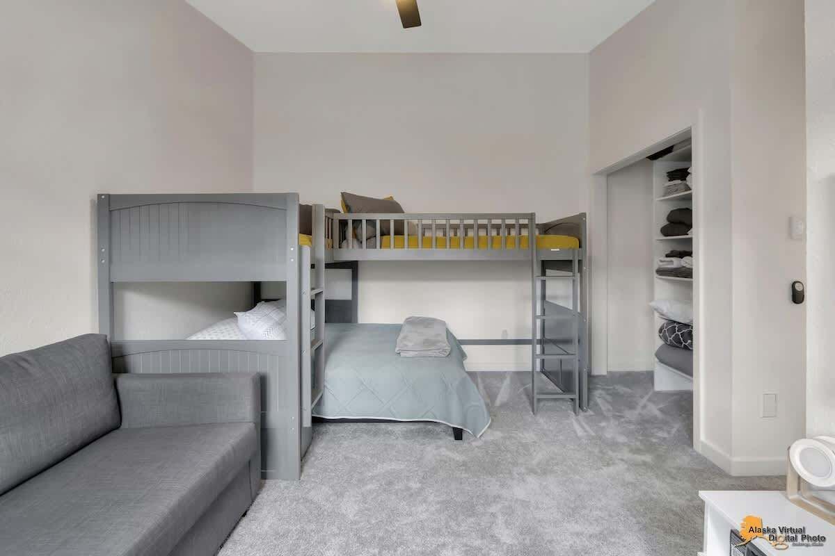 Una habitación compacta con literas, un sofá gris y un armario empotrado.