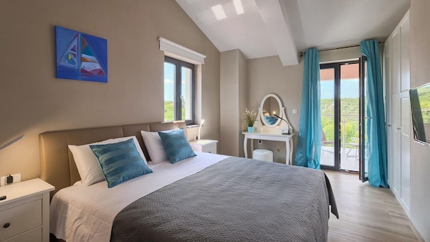 Ein Schlafzimmer mit Bett, Nachttisch und Schreibtisch mit Spiegel. Ein Fenster bietet Blick auf Grünfläche.