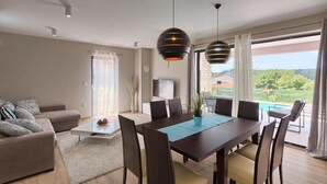 Ein modernes Wohnzimmer mit Essbereich, großen Fenstern und Blick ins Freie.