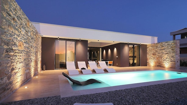 A modern outdoor pool area with lounge chairs and a stone wall. - Beach front home in Kraj (Kraj)