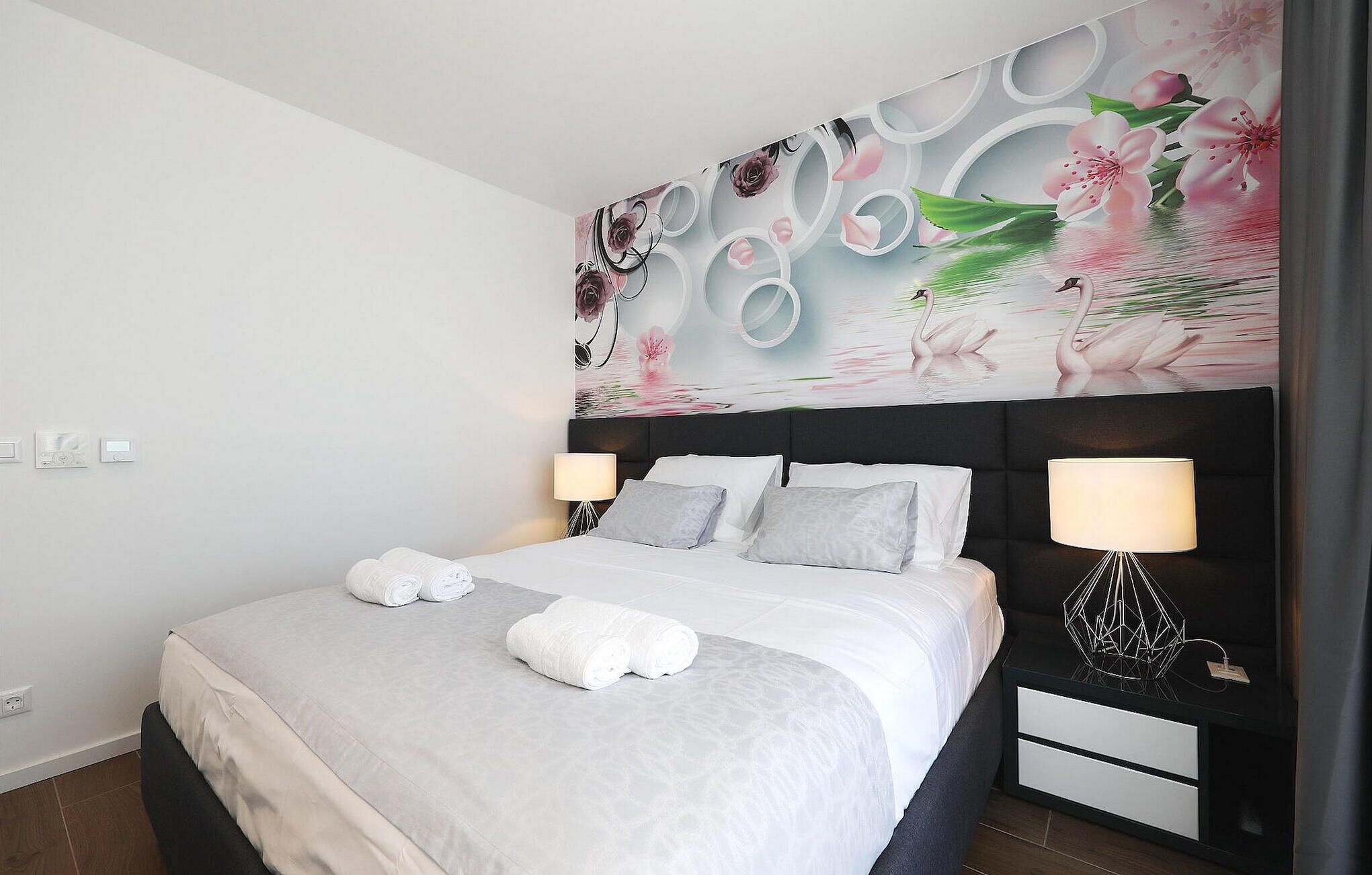A modern hotel room with a large bed, two bedside tables with lamps, and a decorative wall mural.