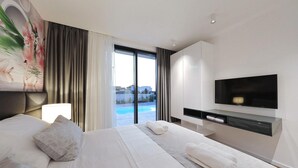 A modern hotel room with a large bed, a flat-screen TV, a view of a swimming pool, and a painting on the wall. - Beach front home in Kraj (Kraj)