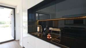 A modern kitchen with a black countertop, stainless steel appliances, and a glass door leading to an outdoor area. - Beach front home in Kraj (Kraj)