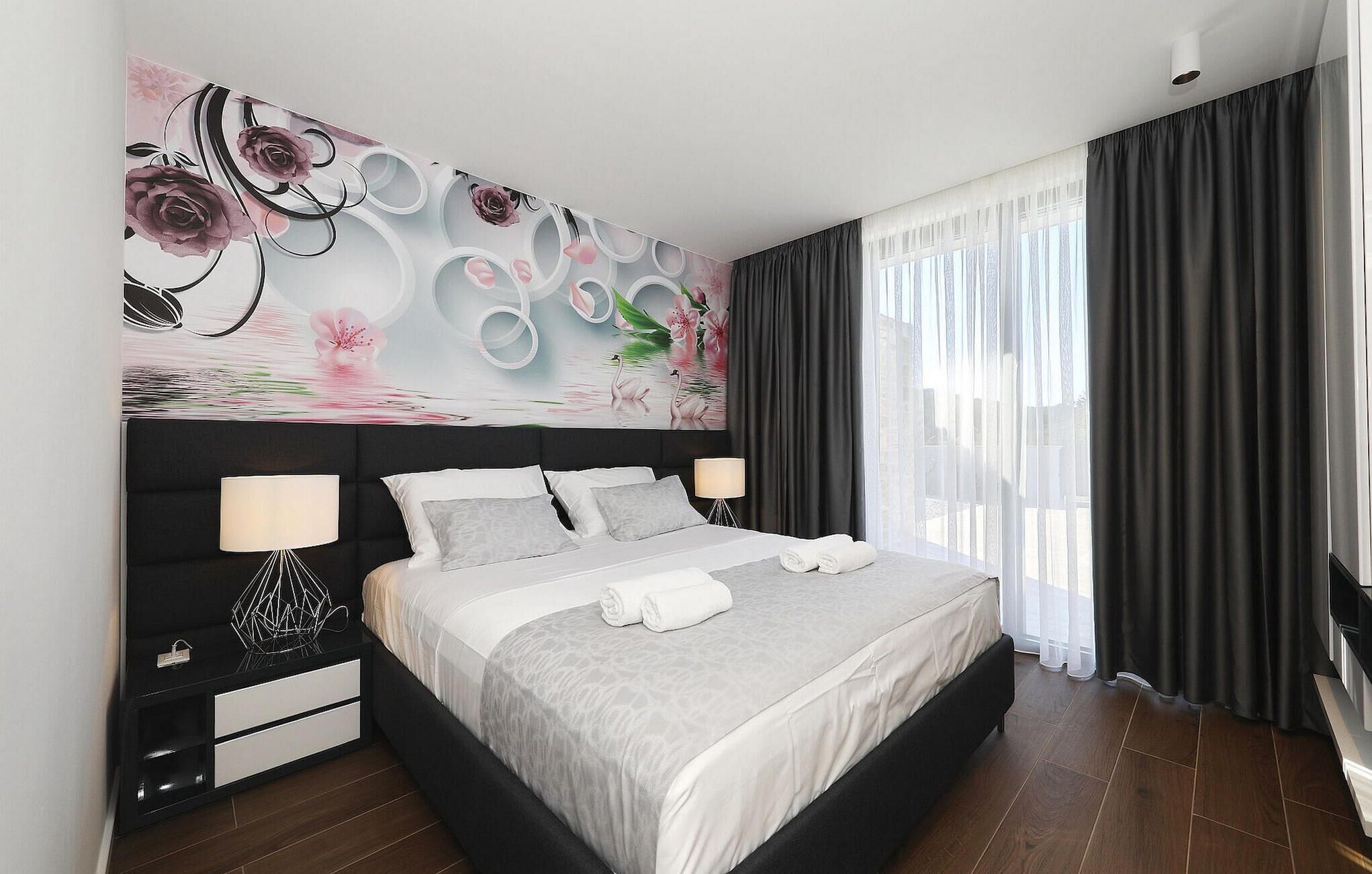 Una habitación de hotel moderna con una cama grande, una mesita de noche con lámpara y un mural decorativo en la pared.