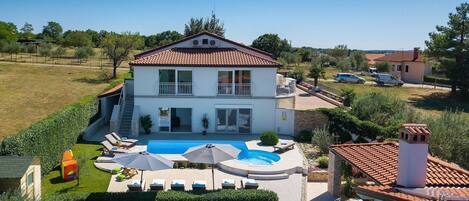 Une maison à deux étages avec une piscine, un espace salon extérieur et un jardin.