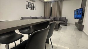 Ein modernes Wohnzimmer mit Essbereich, einem Wand-Fernseher und einer Deckenleuchte.