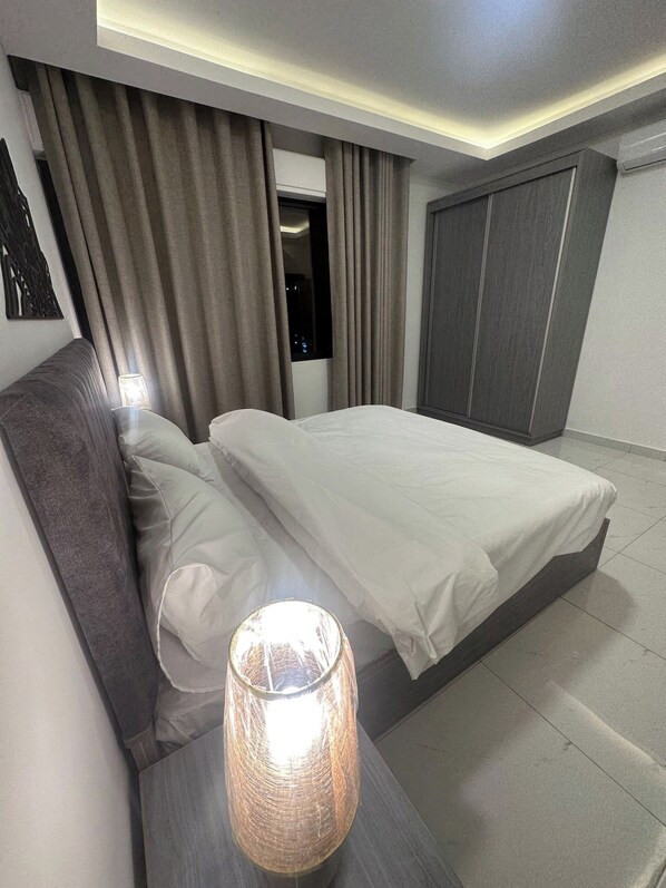 Une chambre d’hôtel moderne équipée d’un lit, de rideaux, d’une table de chevet avec une lampe et d’une armoire.