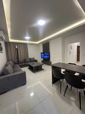 Un salon moderne comprenant un canapé d’angle, une table basse, un téléviseur et un coin repas avec des chaises.
