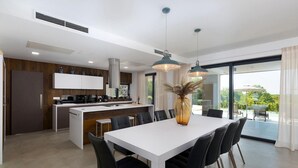 Een moderne keuken met een centraal eiland, een eethoek met een witte tafel en zwarte stoelen, en een groot raam met uitzicht op het groen.
