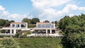 Een modern woongebouw met twee verdiepingen, een terras op het dak, grote ramen en een zwembad.