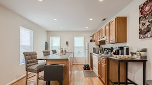 A modern kitchen with wooden cabinets, a central island, and a dining area with chairs. - Baltimore Beauty! Johns Hopkins! Private Parking! (Baltimore)