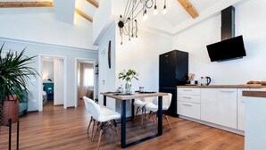 A modern kitchen with a dining area, wooden floors, and a TV mounted on the wall.
