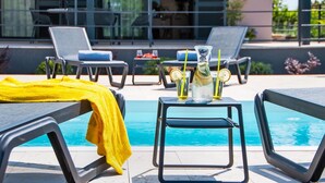 A poolside area with lounge chairs, a table with drinks, and a yellow towel on a chair.