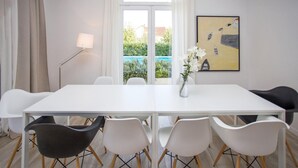 A modern dining room with a white table, six chairs, a vase with flowers, a painting, and a view of a pool through a glass door. - Gorgeous home in Kastel Stafilic (Kastel Stafilic)