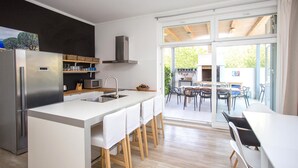 A modern kitchen with a stainless steel refrigerator, a microwave, and a sink. There is a dining area with a table and chairs, and a view of the outdoors through large glass doors. - Gorgeous home in Kastel Stafilic (Kastel Stafilic)