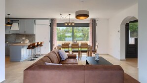 Ein moderner Wohnraum mit braunem Ledersofa, Essbereich mit Holzsesseln und einer Küche mit grauen Schränken.