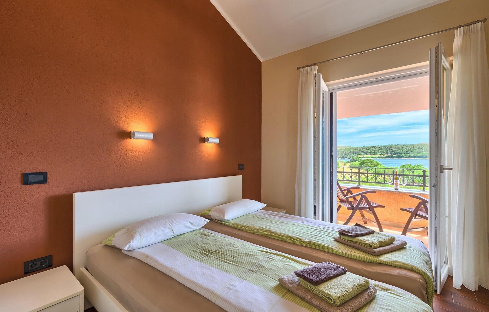 A hotel room with two beds, a balcony with a view of the countryside, and a table with chairs outside.