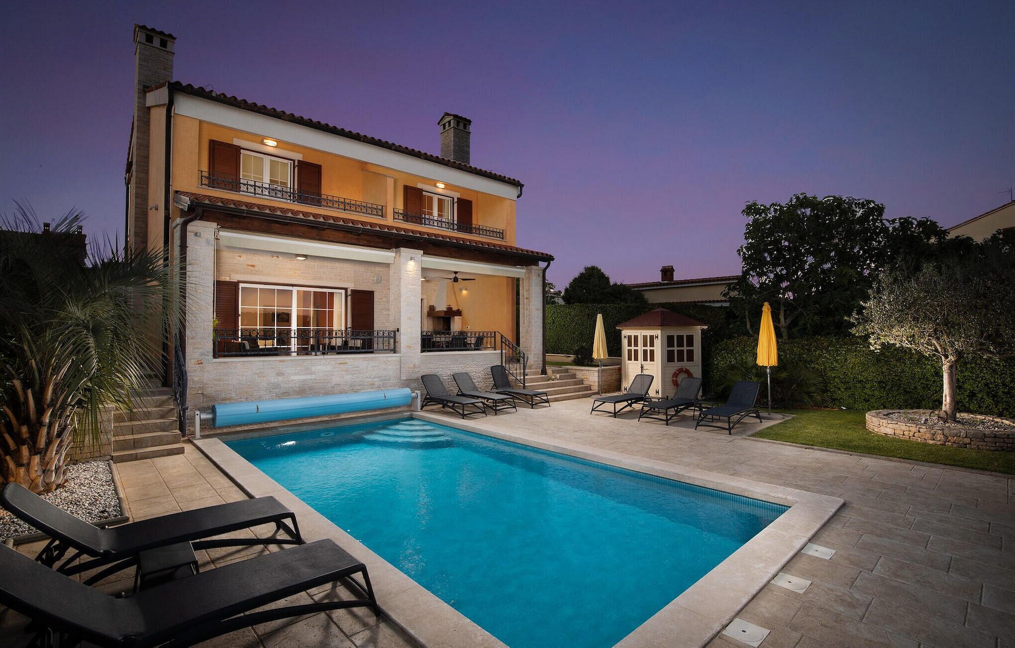 Una casa de dos pisos con piscina, mobiliario exterior y un jardín bien cuidado.
