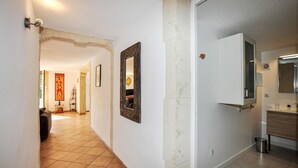 A hallway with a tiled floor, a framed artwork on the wall, and a door leading to a bathroom with a mirror and sink.