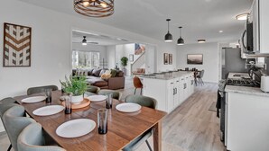 A modern kitchen with white cabinets, a central island, and a dining area with a wooden table set for four. - Poconos Luxury Retreat - Hot-Tub, Billiards, Game Room, Fire-Pit, Private! (Tobyhanna)