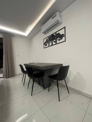 A modern dining area with a dark-toned table and four black chairs, an air conditioning unit, and three framed tree silhouettes on the wall.