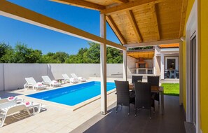 A covered outdoor area with a swimming pool, lounge chairs, and a dining table. - Stunning home in Pula (Pula)