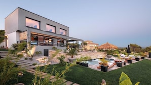 Une maison moderne à deux étages, dotée d’une piscine, d’un espace de détente extérieur et d’un mur en pierre.