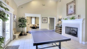 A spacious living room with a ping pong table, a fireplace, and a large plant. - Ocean Walk Condo Upstairs Unit (St. Simons Island)