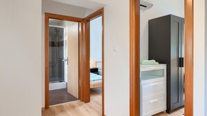 Un pasillo con un marco de puerta de madera, un baño con ducha y un armario blanco con una toalla verde.