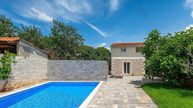 Una piscina con paredes de piedra, un sendero de piedra y un edificio con tejado de azulejos al fondo.