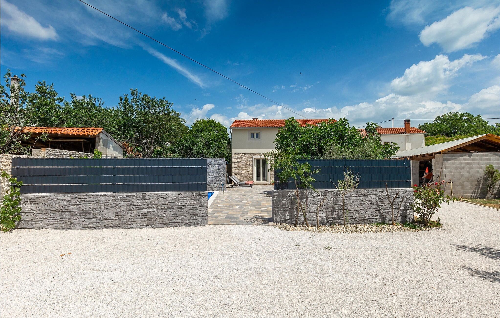 A residential property with a stone wall entrance, a paved driveway, and a red-tiled roof house.