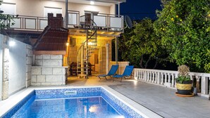 En swimmingpool med en stenmur på ena sidan och ett takförsett utomhusområde med en spiraltrappa.