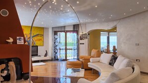 A modern living room with a white sofa, a coffee table, and a large floor lamp. There is a painting on the wall and a window with curtains. - Nice home in Labin - Rabac (Labin - Rabac)