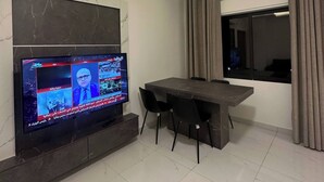 Ein modernes Wohnzimmer mit Flachbildfernseher an der Wand, einem Esstisch mit Stühlen und einer Klimaanlage.