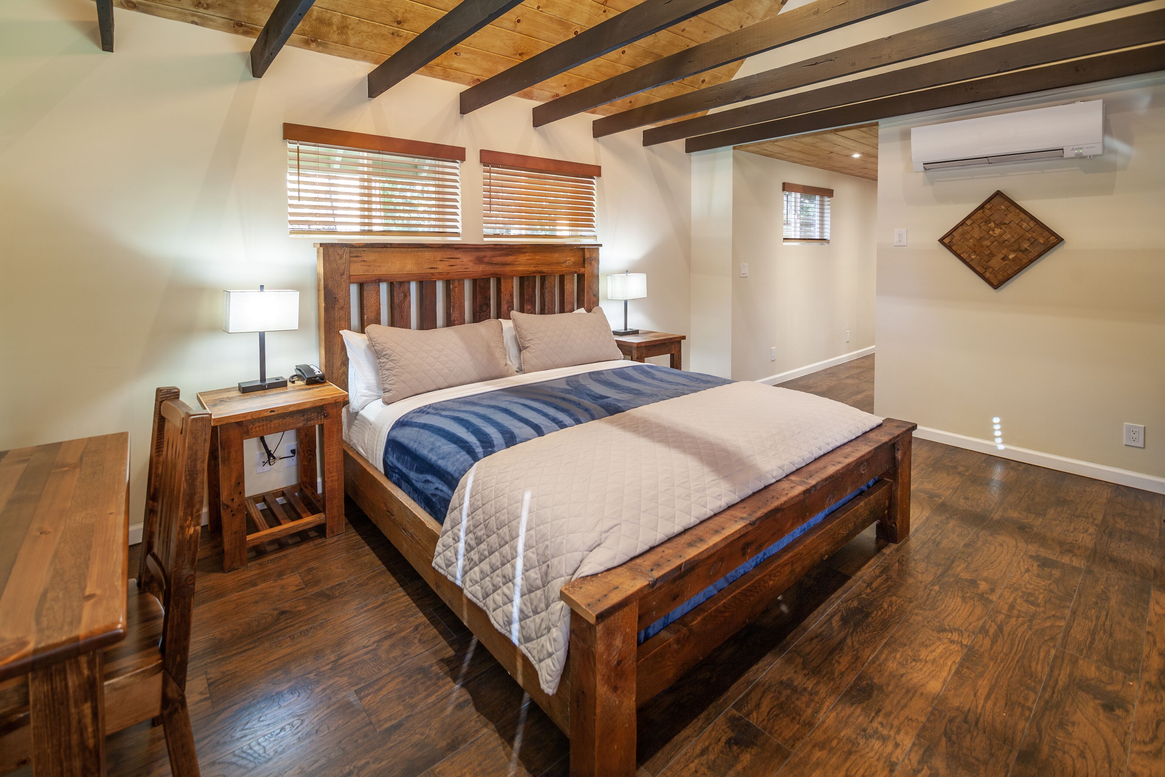 Quarto com cama de madeira, mesas de cabeceira, um banco e teto de madeira.