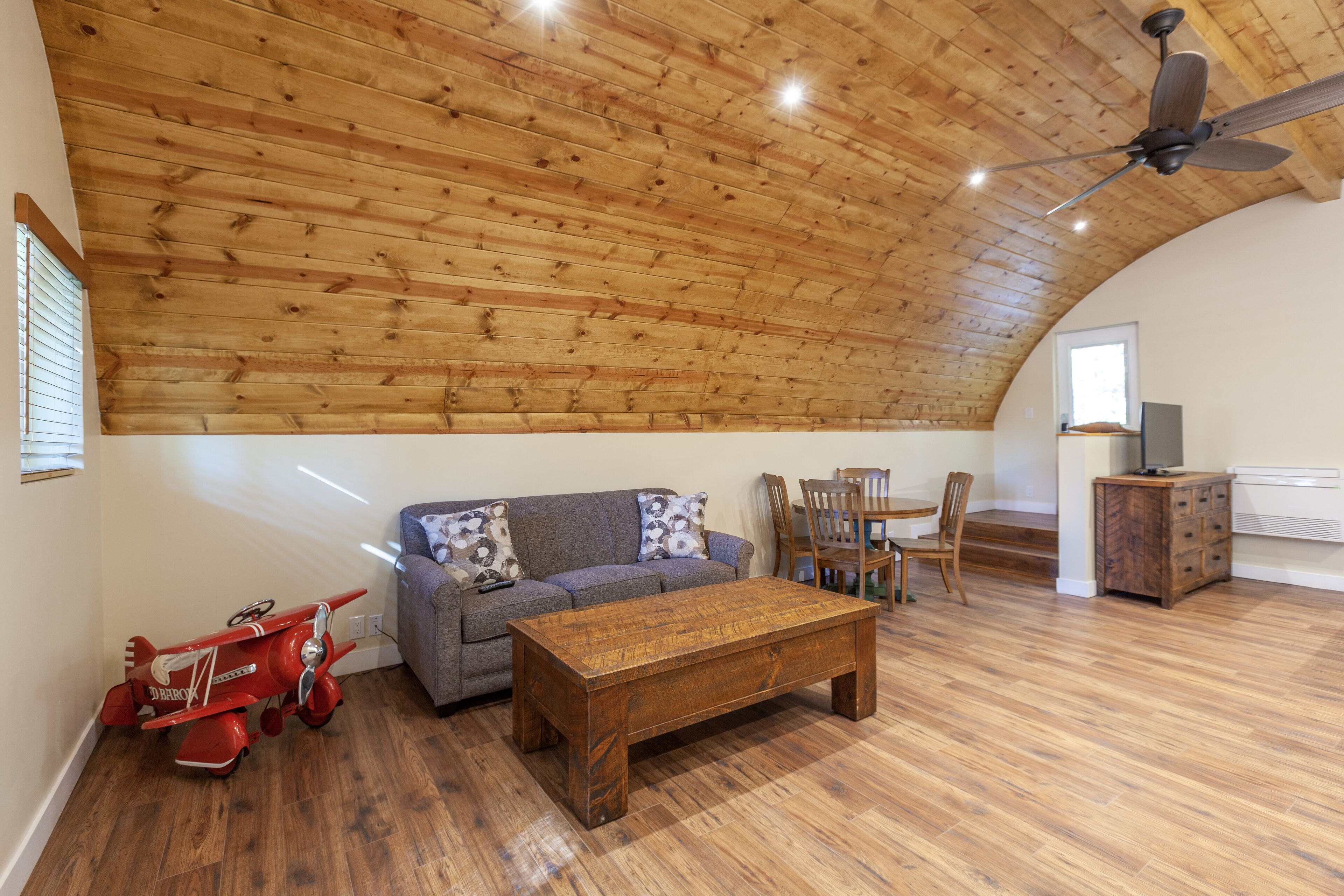 A spacious living area with a wooden ceiling, a sofa, a coffee table, and a red toy airplane.