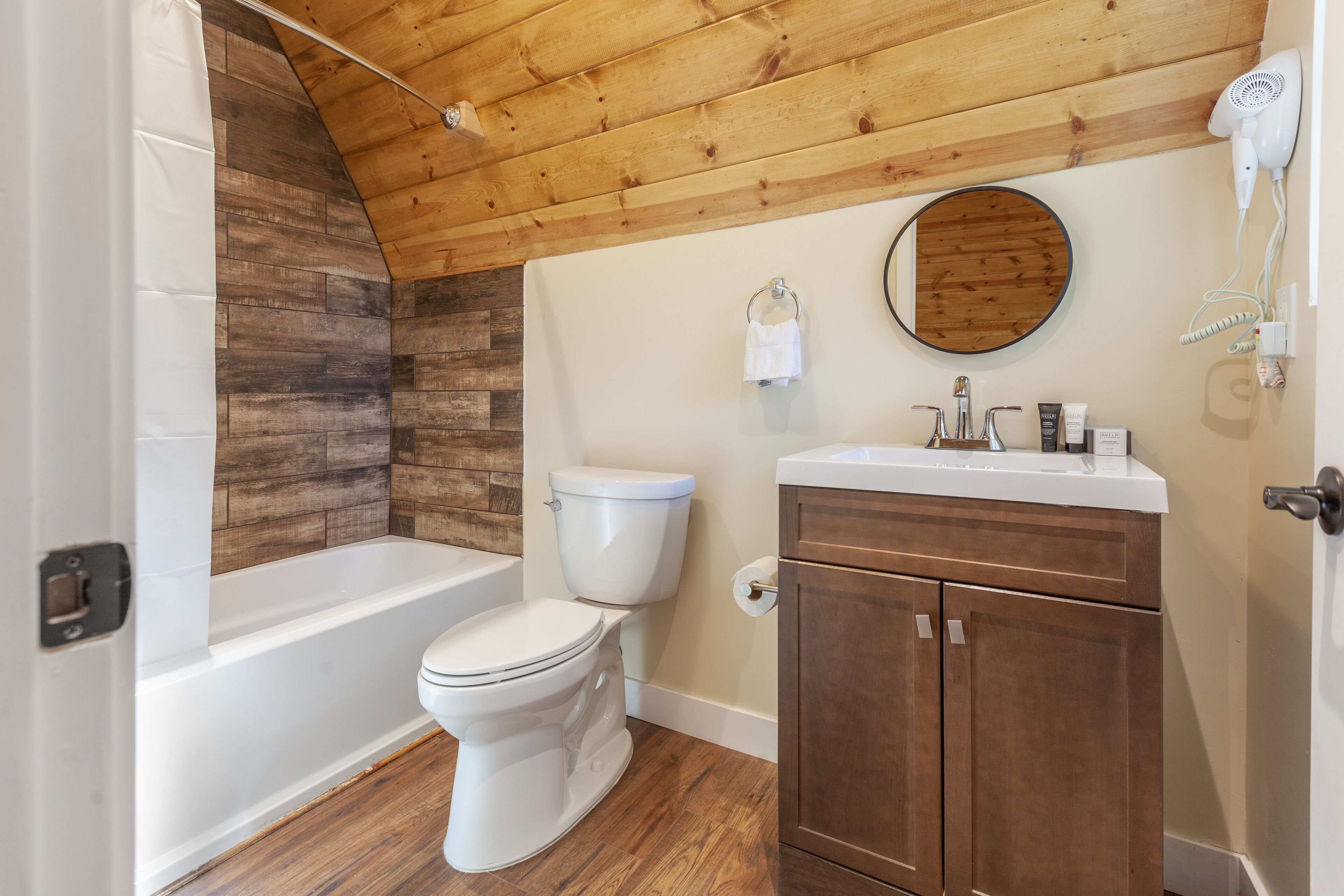 A bathroom with a wooden ceiling, a white toilet, a bathtub, and a wooden vanity with a mirror.