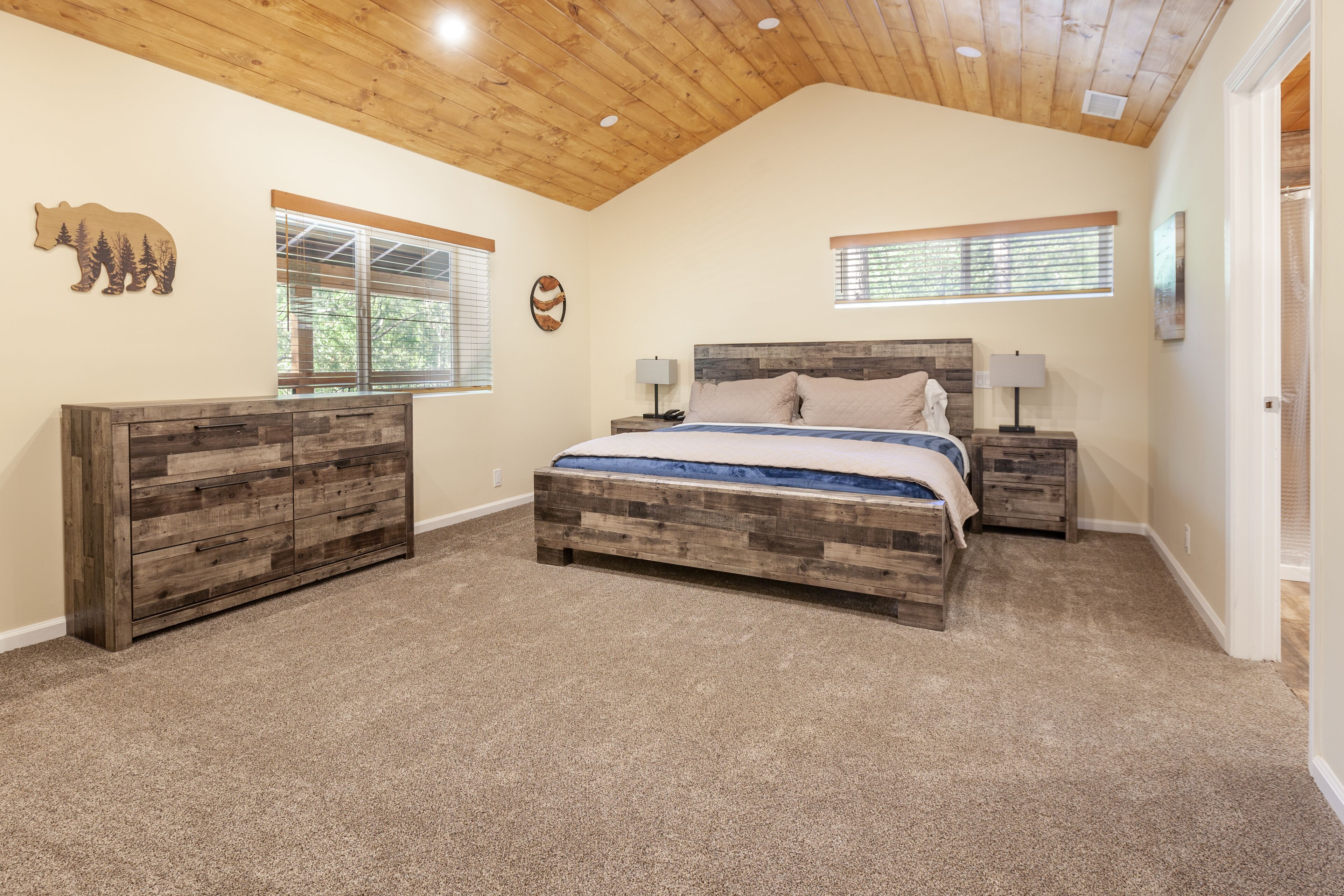 A bedroom with a wooden headboard bed, two bedside tables with lamps, a dresser, and a ceiling with wooden beams.