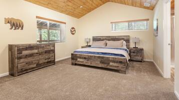 A bedroom with a wooden headboard bed, two bedside tables with lamps, a dresser, and a ceiling with wooden beams.