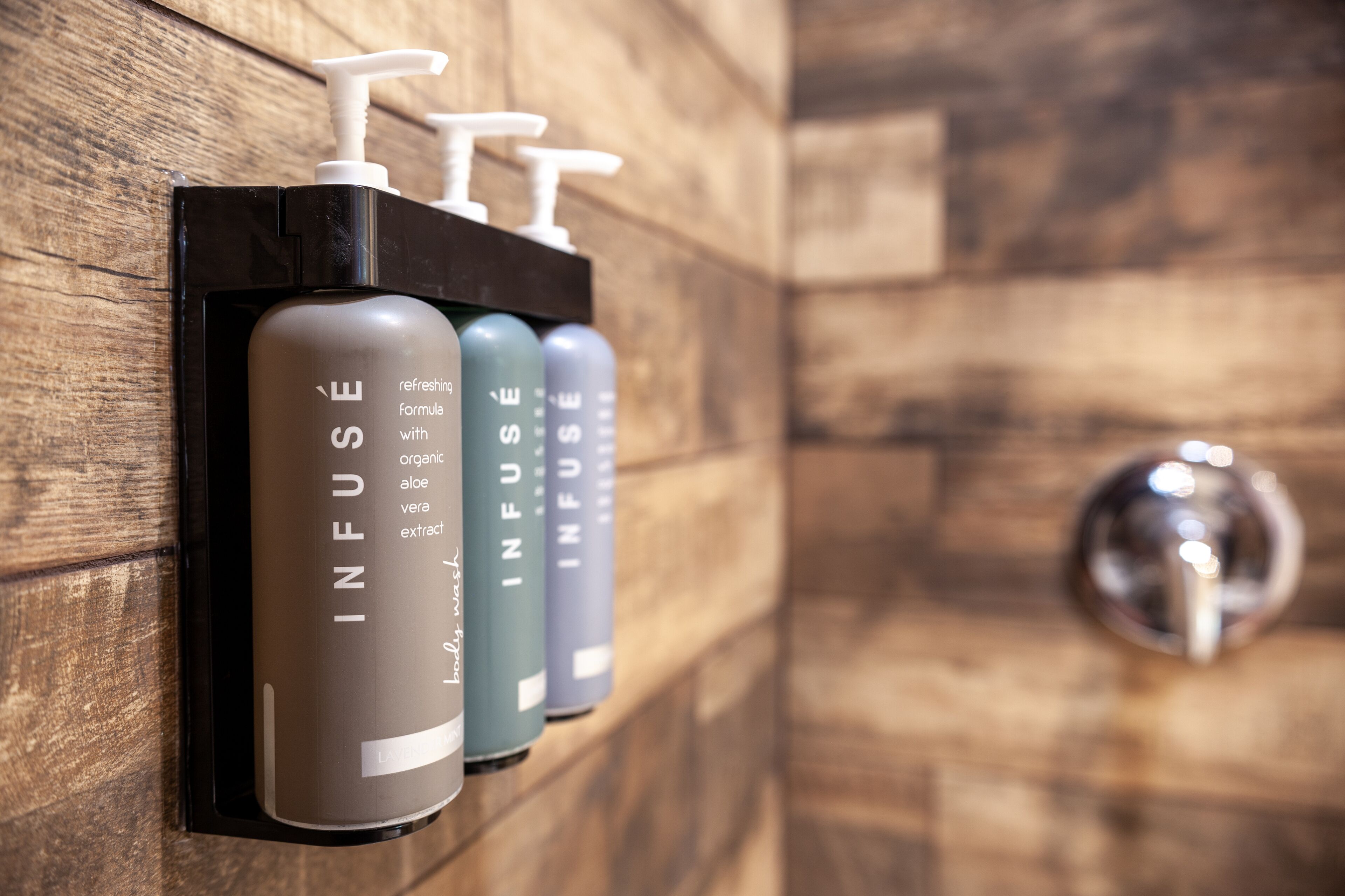 A wall-mounted dispenser with three bottles labeled "INFUSE" for a refreshing formula with organic aloe vera extract.