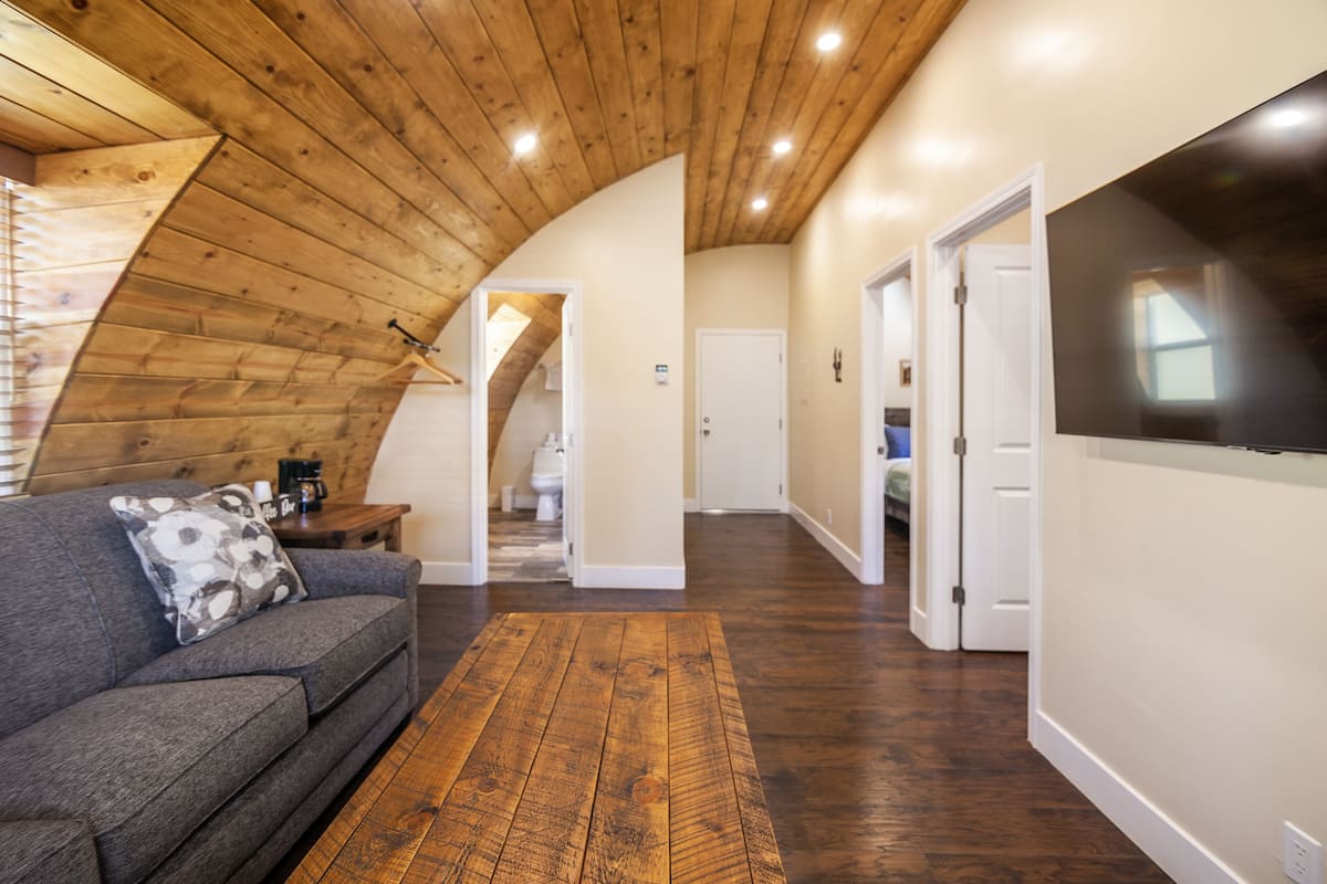 A modern interior with a wooden ceiling, a grey sofa with a patterned pillow, and a wooden floor.