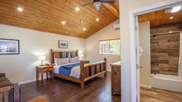 Ein Schlafzimmer mit Holzboden, einem Bett mit Kopfteil, Nachttischen und Blick auf ein Badezimmer mit Holzwand.