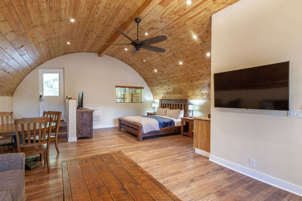 A bedroom with a wooden ceiling, a bed, a desk, and a TV mounted on the wall.