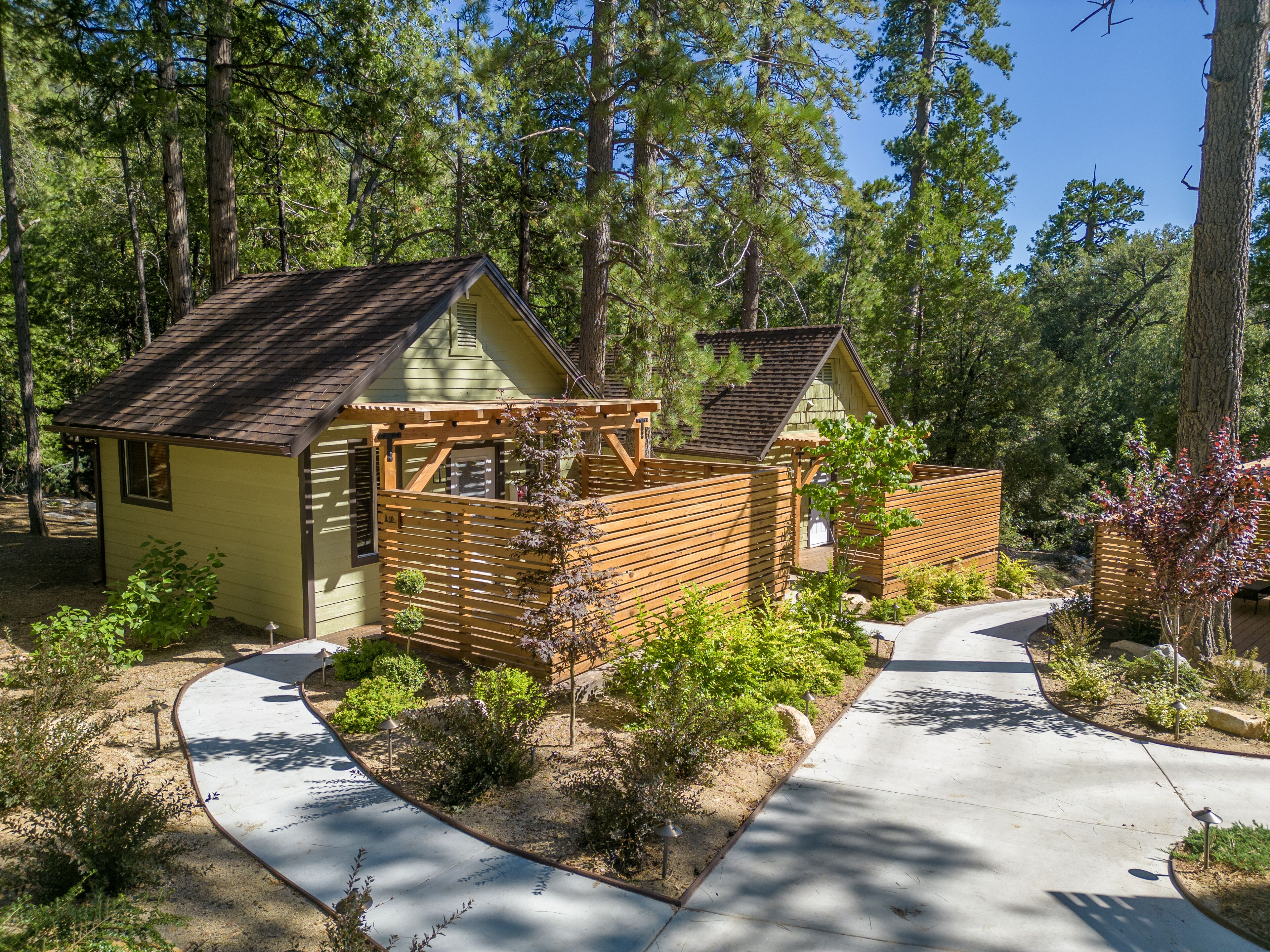 A small, yellow cabin with a wooden deck and a covered porch, surrounded by dense forest.