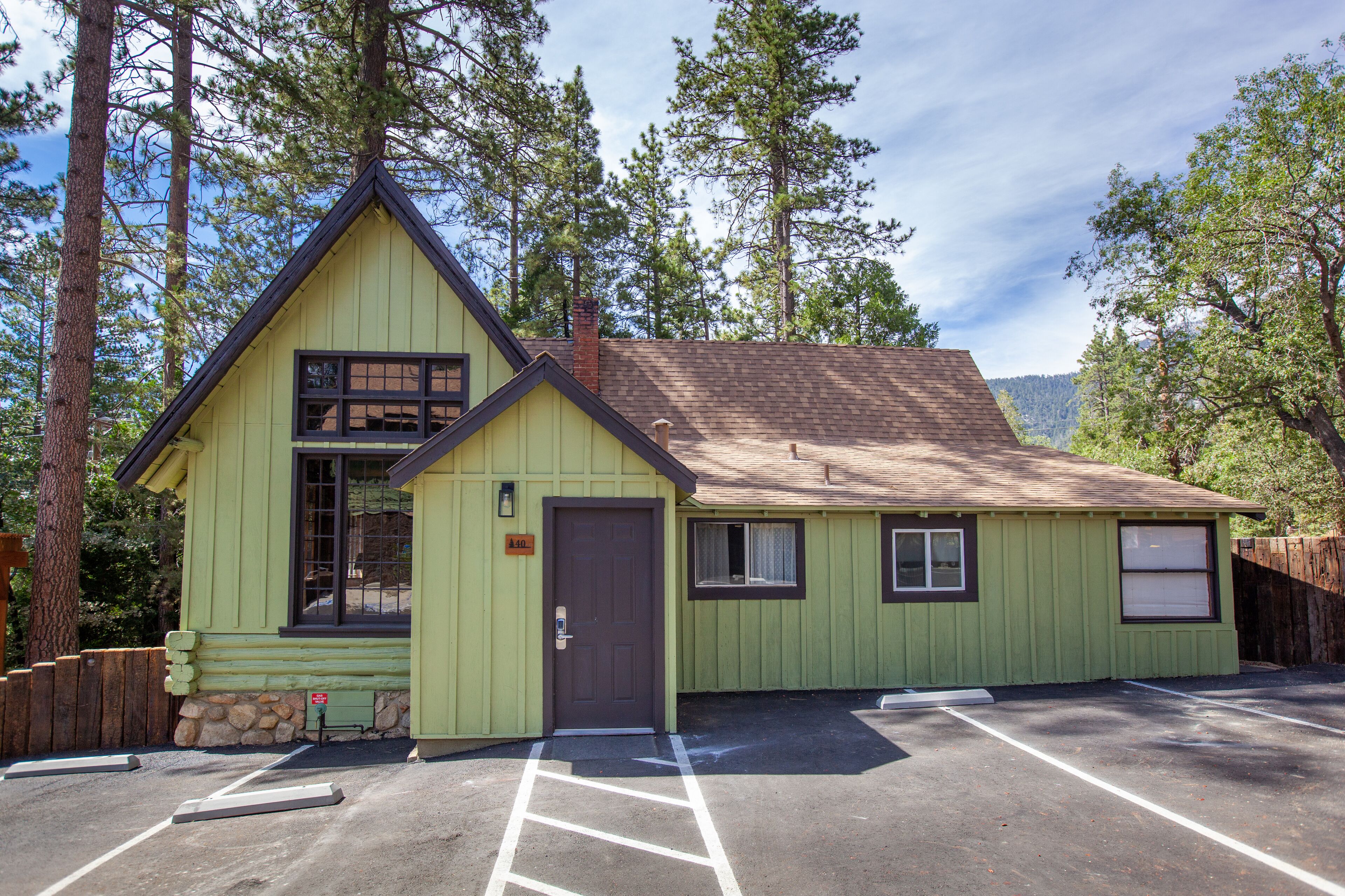 A green lodge with a brown door and windows, a stone foundation, and a parking lot.